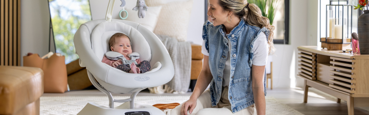 Mum smiling at baby girl buckled in to the Graco Eluma Sway soothing baby swing.